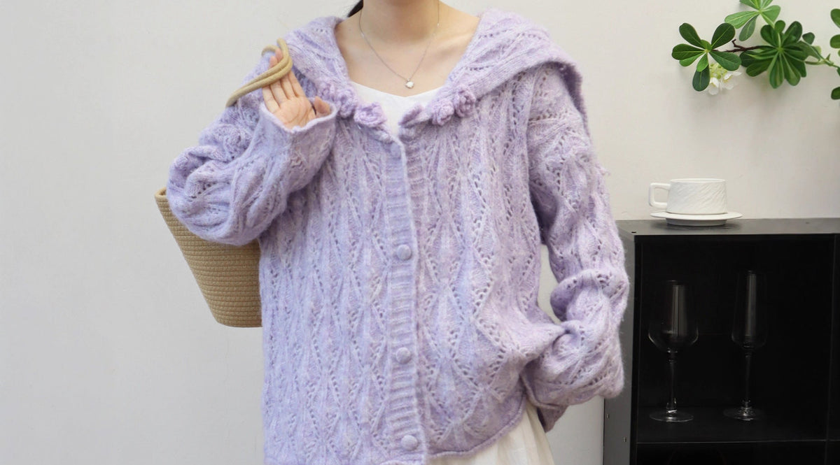Person wearing a light purple knitted cardigan over a white dress, standing indoors.
